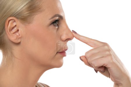 Foto de Perfil od una mujer seria de mediana edad touchinf su nariz en un fondo de estudio blanco - Imagen libre de derechos