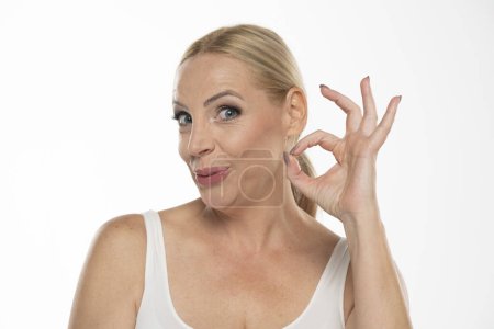 Photo for Portrait of senior middle aged blond woman showing delicious sign on white studio background - Royalty Free Image