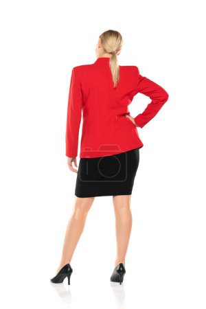 Téléchargez les photos : Femme d'affaires senior d'âge moyen en veste rouge et jupe noire posant sur fond de studio blanc. Arrière, vue arrière. - en image libre de droit