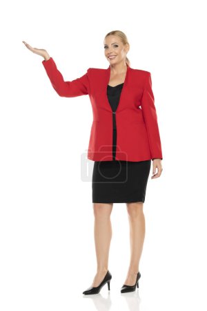 Foto de Mujer de mediana edad de publicidad senior de negocios en chaqueta roja y falda negra posando sobre fondo de estudio blanco. Vista frontal. - Imagen libre de derechos