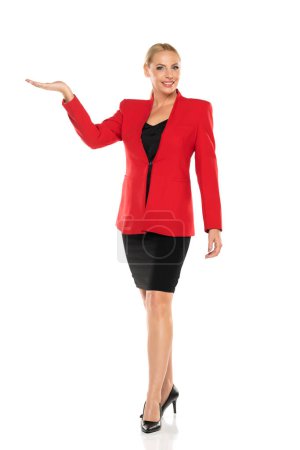 Foto de Mujer de mediana edad de publicidad senior de negocios en chaqueta roja y falda negra posando sobre fondo de estudio blanco. Vista frontal. - Imagen libre de derechos