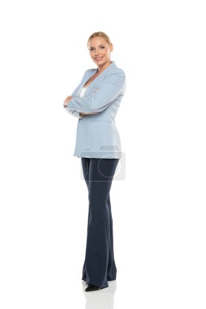 Téléchargez les photos : Femme âgée souriante d'âge moyen portant une veste bleue et un pantalon noir sur fond de studio blanc - en image libre de droit