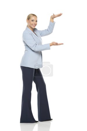 Foto de Mujer de mediana edad de publicidad senior de negocios en chaqueta azul y pantalones negros posando sobre fondo de estudio blanco.. - Imagen libre de derechos