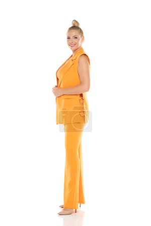 Photo for Middle aged smiling senior woman in yellow sleevless jacket and trousers posing on a white studio background - Royalty Free Image