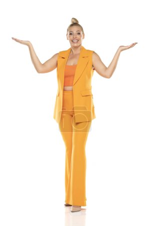 Photo for Middle aged advertising senior business woman in yellow sleeveless jacket and trousers posing on white studio background. Front view. - Royalty Free Image