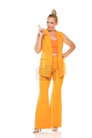 Photo for Middle aged senior woman in yellow sleevless jacket and trousers pointing up on a white studio background - Royalty Free Image