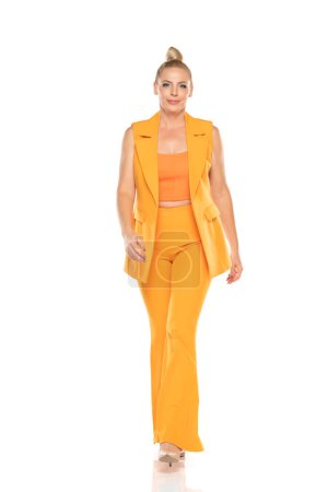 Photo for Middle aged senior woman in yellow sleevless jacket and trousers walking on a white studio background - Royalty Free Image