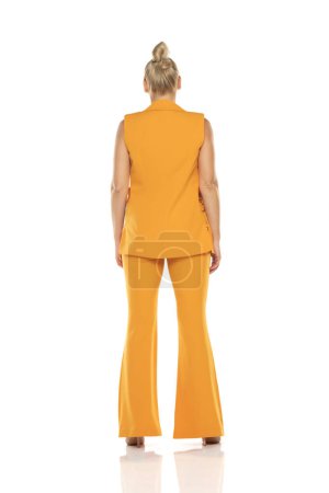 Photo for Middle aged senior woman in yellow sleevless jacket and trousers posing on a white studio background. Back, rear view. - Royalty Free Image