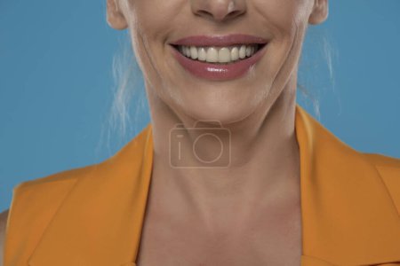 Téléchargez les photos : Dents en porcelaine dans la bouche souriante féminine sur fond de studio bleu - en image libre de droit