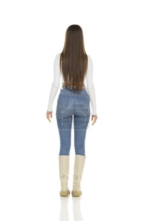 Photo for Back, rear view of a young woman in white shirt, blue jeans and boots on a white studio background - Royalty Free Image