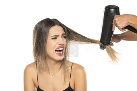 Photo for Hairdresser inflicts pain on a young woman drying her hair on a white studio background - Royalty Free Image