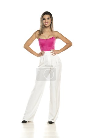 Photo for Young modern smiling woman in white pants and pink corset posing on white studio background - Royalty Free Image