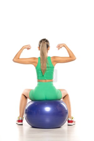 Foto de Vista trasera de una mujer joven y deportiva en pantalones cortos verdes y la parte superior posando en la pelota de fitness sobre fondo de estudio blanco - Imagen libre de derechos