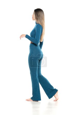 Téléchargez les photos : Jeune femme pieds nus moderne en pantalon bleu et chemisier marchant sur fond de studio blanc. côté, vue de profil - en image libre de droit