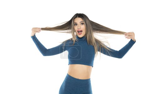 Téléchargez les photos : Jeune femme excitée tenant ses cheveux longs sur un fond de studio blanc - en image libre de droit
