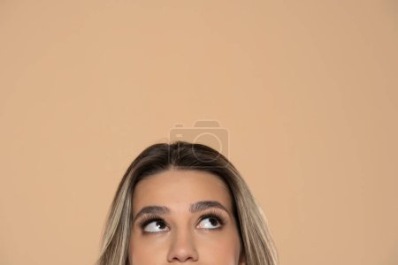 Téléchargez les photos : Demi portrait d'une jeune fille regardant vers le haut sur un fond de studio beige - en image libre de droit