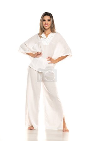 Foto de Joven mujer sonriente desnuda moderna en pantalones blancos y blusa posando sobre fondo blanco del estudio. vista frontal - Imagen libre de derechos
