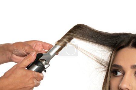 Téléchargez les photos : Styliste utilisant du fer à friser pour boucles de cheveux, gros plan, isolé sur fond de studio blanc - en image libre de droit