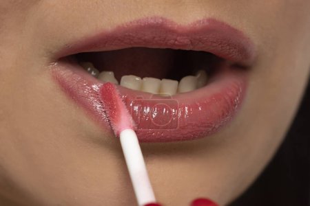 Téléchargez les photos : Gros plan femme appliquant rose hydratant brillant à lèvres sur ses lèvres. Maquillage parfait. - en image libre de droit