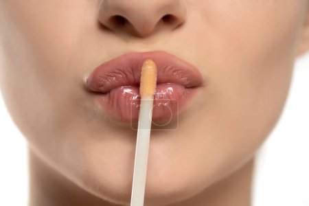 Téléchargez les photos : Jeune belle femme appliquer un brillant à lèvres sur ses lèvres sur fond de studio blanc - en image libre de droit