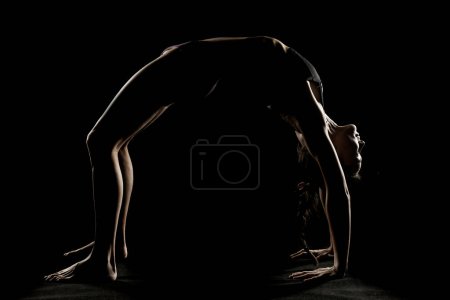 Photo for Art silhouette of a young woman doing yoga exercise. Yoga pose on black studio background. - Royalty Free Image