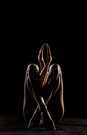 Téléchargez les photos : Silhouette de femme nue méconnaissable posant dans l'ombre sur un fond de studio noir - en image libre de droit