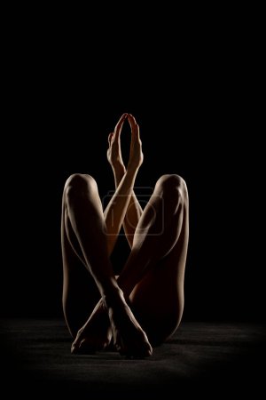 Foto de Silueta de mujer desnuda irreconocible posando en las sombras sobre un fondo de estudio negro - Imagen libre de derechos