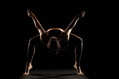 Foto de Silueta artística de una joven haciendo ejercicio de yoga. Postura de yoga sobre fondo de estudio negro. - Imagen libre de derechos