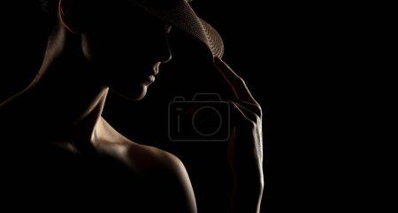 Téléchargez les photos : Portrait sensuel silhouette de belle femme avec un chapeau en contre-jour sur un fond de studio noir - en image libre de droit