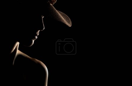 Foto de Sensual silueta de retrato de mujer hermosa con un sombrero en contraluz sobre un fondo de estudio negro - Imagen libre de derechos