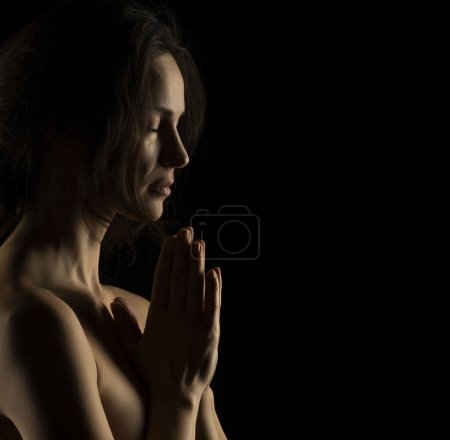 Téléchargez les photos : Silhouette de jeune femme priante sur fond de studio noir - en image libre de droit