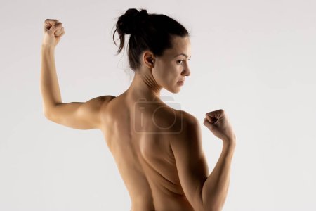 Foto de Mujer joven atlética en la sombra que muestra los músculos de la espalda y las manos sobre un fondo blanco aislado estudio - Imagen libre de derechos