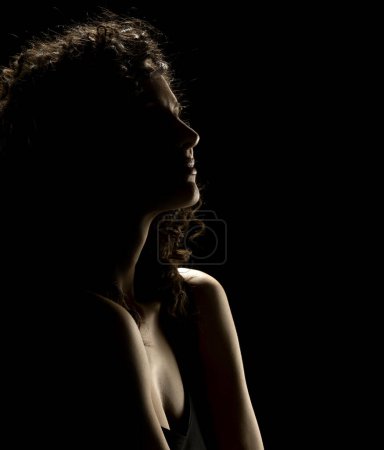 Foto de Sensual silueta de retrato de hermosa mujer rizada en contraluz sobre un fondo de estudio negro - Imagen libre de derechos
