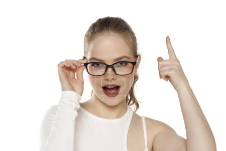 Photo for Portrait of beautiful positive blonde woman wearing glasses and pointing up on a white background - Royalty Free Image