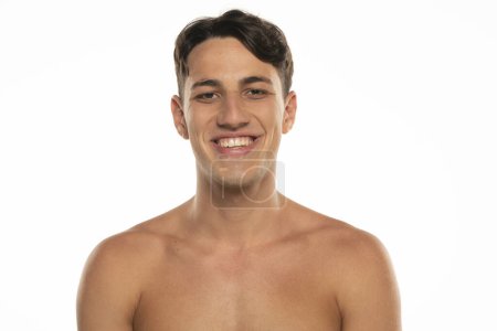 Téléchargez les photos : Gros portrait d'un homme souriant et torse nu dans la vingtaine regardant une caméra isolée sur un fond de studio blanc - en image libre de droit