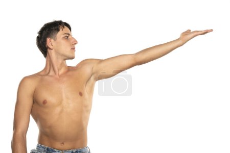 Foto de Hombre musculoso con el brazo extendido. modelo de moda joven en topless con su mano en el aire. Aislado sobre un fondo de estudio blanco - Imagen libre de derechos
