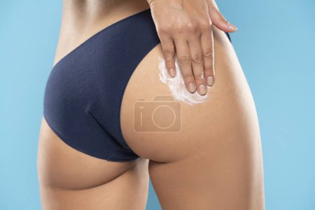 Photo for Cropped shot of slim young woman in underwear applying body cream on her bottom on a blue studio background - Royalty Free Image