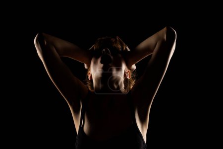 Foto de Retrato de una mujer gritando en la sombra, sosteniendo su cabeza, ojos cerrados sobre un fondo negro del estudio - Imagen libre de derechos