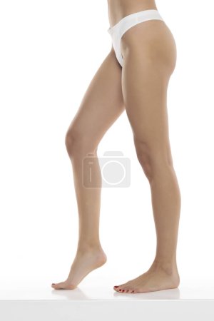 Téléchargez les photos : Jambes féminines parfaites en sous-vêtements sur fond de studio blanc. Côté, vue de profil - en image libre de droit