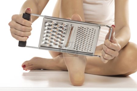Photo for A woman scrapes her feet with a kitchen grater on a white studio background - Royalty Free Image
