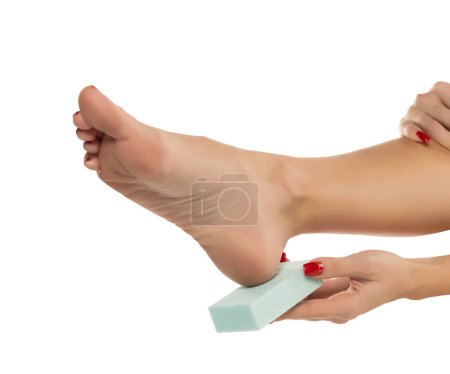 Téléchargez les photos : Woman file her feet with a pumice stone on white studio background - en image libre de droit