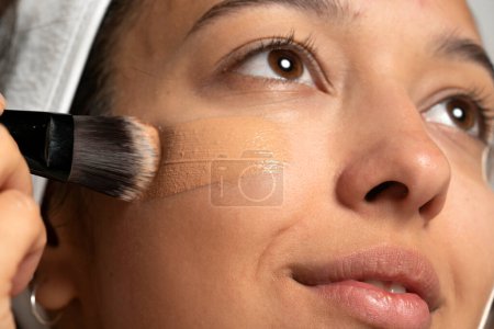 Photo for Young etnic woman applyes liquid founation on her face with makeup brush on white studio  background - Royalty Free Image
