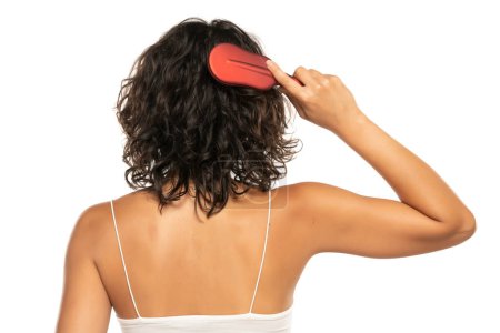 Téléchargez les photos : Vue arrière plan de la tête de la femme peigner ses cheveux ondulés foncés bouclés sur fond de studio blanc - en image libre de droit