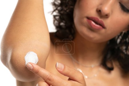 Photo for Head shot of a exotic woman takes care of her elbows using cosmetic cream on a white studio background - Royalty Free Image