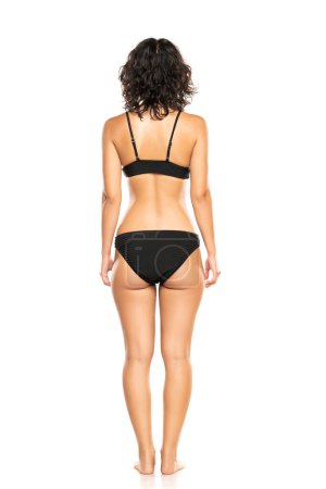 Photo for Young brunette woman in black bikini swimsuit posing on a white studio background. Back, rear view. - Royalty Free Image