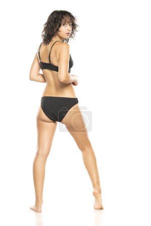 Foto de Joven mujer morena exótica en bikini negro posando sobre un fondo de estudio blanco. Atrás, vista trasera. - Imagen libre de derechos