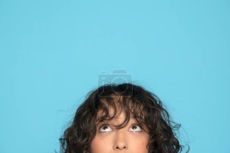 Photo for Closeup portrait headshot cropped face above lips of cute happy woman looking up isolated on blue studio wall background with copy space above head. - Royalty Free Image