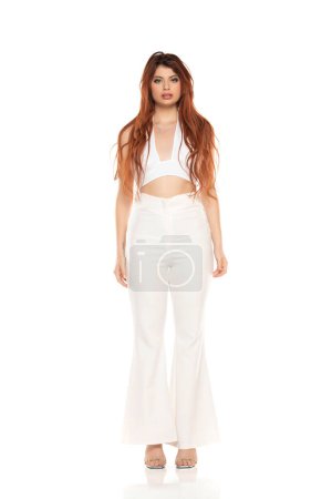 Photo for Fashion style studio portrait of beautiful young woman. White wide leg pants and white sleevles shirt. Model standing and posing against white studio background - Royalty Free Image