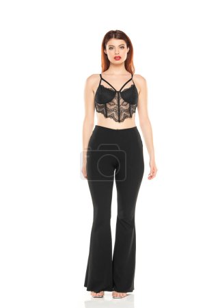 Photo for Fashion style studio portrait of beautiful young woman. Black wide leg pants and black lace bra. Model standing and posing against white studio background - Royalty Free Image