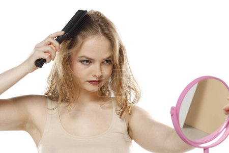 Téléchargez les photos : Belle femme blonde brossant les cheveux avec peigne sur un fond de studio blanc - en image libre de droit
